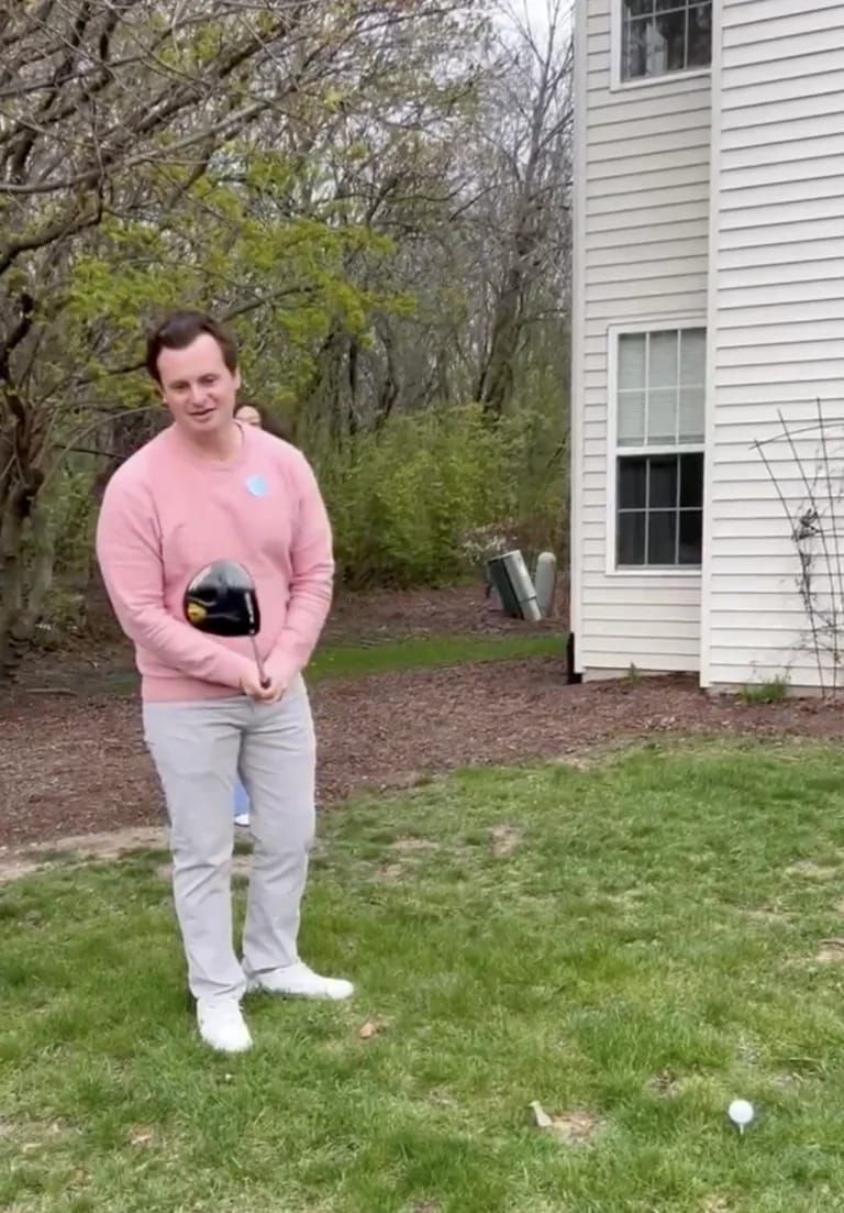 Tom Dillon standing on a backyard lawn holding a golf driver, preparing to hit a gender reveal golf ball
