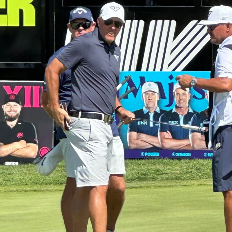 Professional golfer at a tournament warming up on the green, Majors event signage and other golfers visible in the background